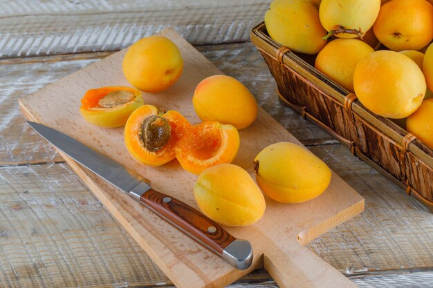 Abricots avec couteau dans un panier sur planche de bois et à découper, vue du dessus.