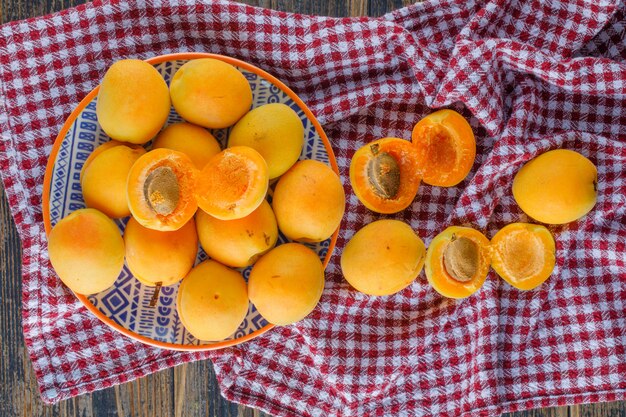 Abricots dans une assiette à plat sur un tissu de pique-nique et une table en bois