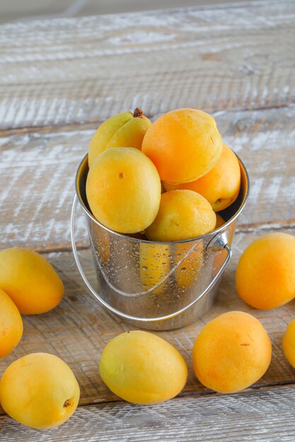 Abricots dans un mini seau sur table en bois, vue du dessus.