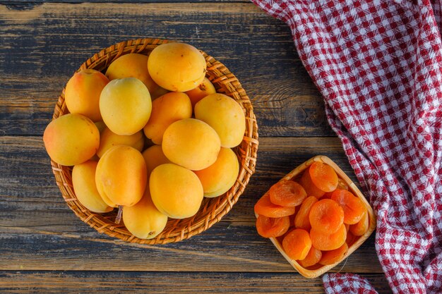 Abricots dans un panier en osier avec des abricots secs à plat poser sur un tissu de pique-nique et table en bois