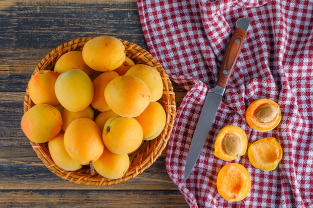 Abricots dans un panier en osier avec un couteau à plat sur un tissu de pique-nique et une table en bois