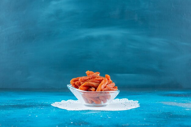 Abricots secs dans un bol sur des dessous de verre sur la surface bleue