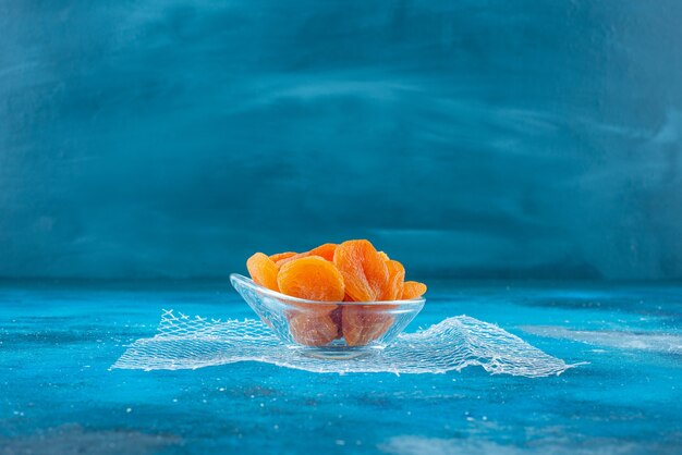 Abricots secs dans un bol en verre, sur la table bleue.