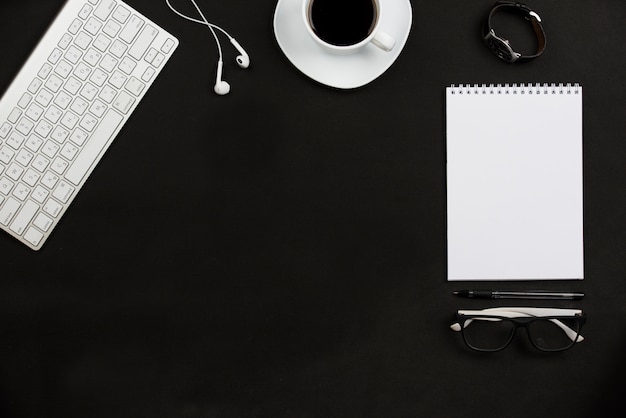 Accessoires personnels; tasse à café; écouteur; lunettes et clavier sur fond noir