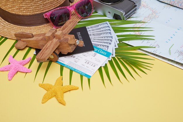 Accessoires de voyageurs laïcs plats sur une surface jaune avec feuille de palmier, appareil photo, chaussure, chapeau, passeports, argent, billets d'avion, avions et lunettes de soleil. Vue de dessus, concept de voyage ou de vacances.
