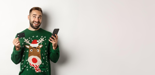 Photo gratuite achats en ligne du nouvel an et concept de noël jeune homme achetant des cadeaux sur internet tenant une pho mobile