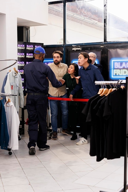 Photo gratuite des acheteurs émotifs et impatients faisaient la queue à l'extérieur du grand magasin, se disputant avec un agent de sécurité du magasin de vêtements qui patrouillait à l'entrée, des gens en colère fatigués d'attendre les offres du black friday dans une longue file d'attente