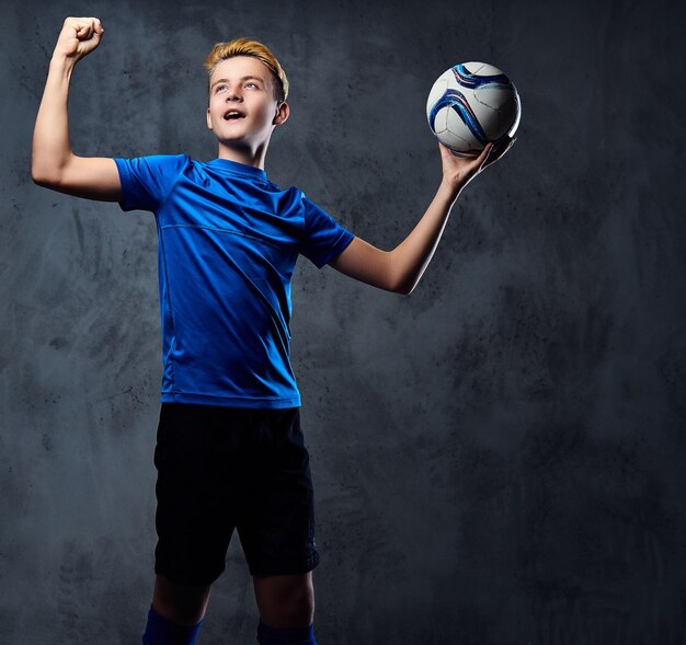 Adolescent blond, joueur de football vêtu d'un uniforme bleu tient une balle.