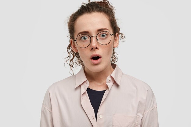 Adolescent choqué de taches de rousseur avec des lunettes posant contre le mur blanc