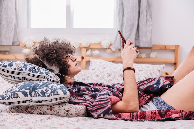 Photo gratuite adolescent dans les écouteurs en utilisant le smartphone sur le lit