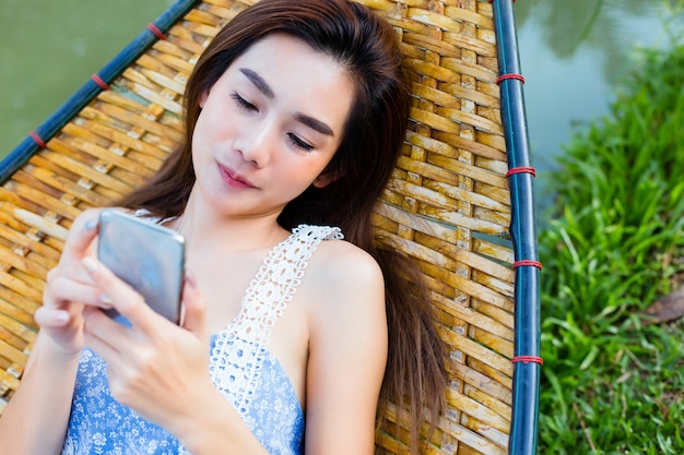 Adolescent femelle allongée sur un hamac en bambou à l'aide de smartphone