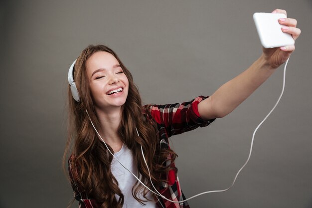 Adolescent fille joyeuse prenant selfie et écouter de la musique avec des écouteurs