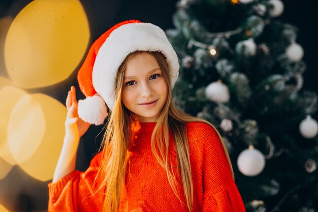 Adolescent fille mignonne en bonnet de Noel rouge par arbre de Noël