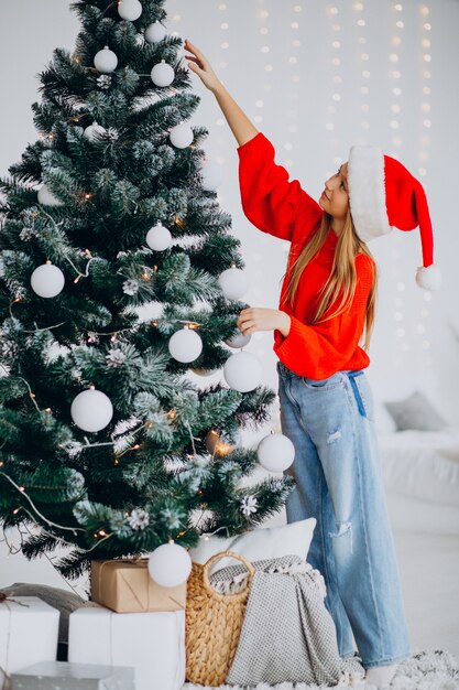 Adolescent fille mignonne en bonnet de Noel rouge par arbre de Noël