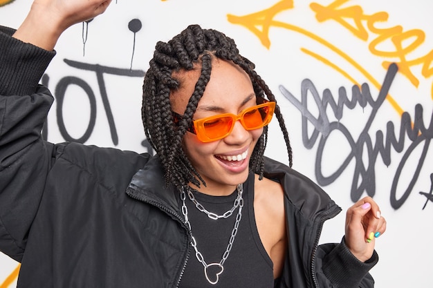 Photo gratuite adolescent heureux avec des danses de coiffure à la mode contre le mur de graffitis dessiné.