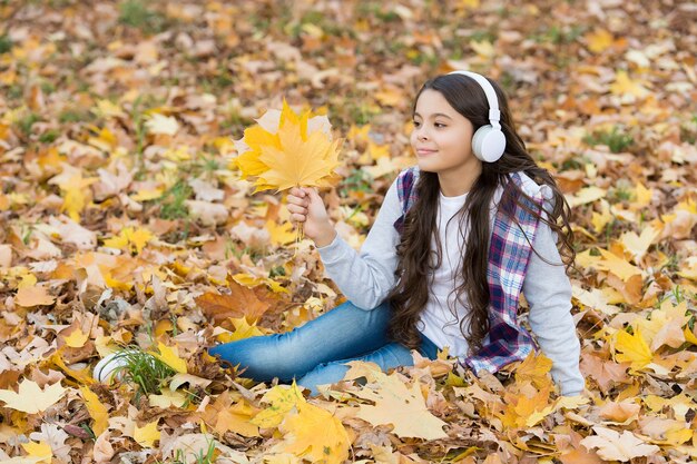 Un adolescent heureux écoute de la musique avec des écouteurs dans la forêt d'automne avec une belle nature saisonnière ou une leçon en ligne, une technologie moderne.