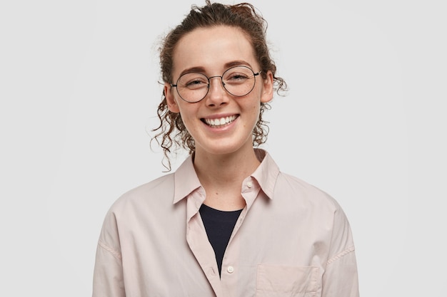 Adolescent heureux avec des taches de rousseur posant contre le mur blanc