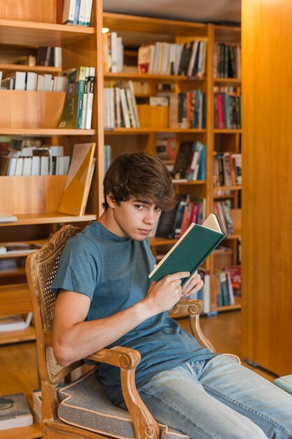 Adolescent avec livre assis dans la bibliothèque