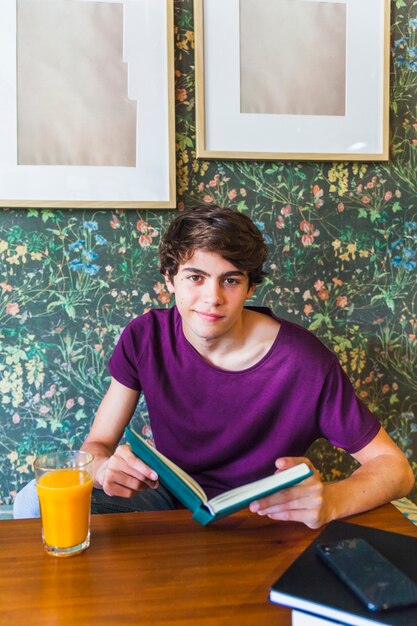 Adolescent avec livre assis sous les cadres au café