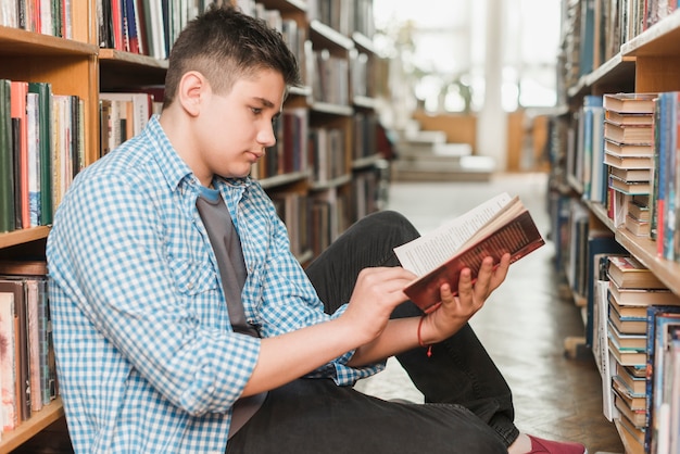 Adolescent mâle lisant un livre sur le sol