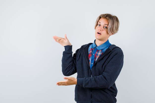 Adolescent mignon en chemise, sweat à capuche montrant un signe de grande taille et se demandant, vue de face.