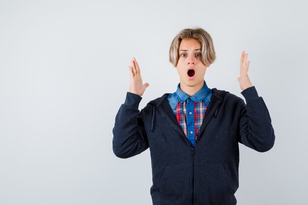 Adolescent mignon en chemise, sweat à capuche montrant un signe de grande taille et se demandant, vue de face.