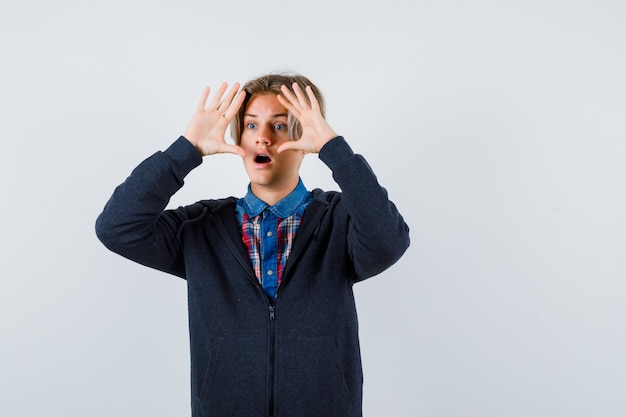 Adolescent Mignon Regardant Loin Avec Les Mains Au-dessus De La Tête En Chemise, Sweat à Capuche Et L'air étonné. Vue De Face.