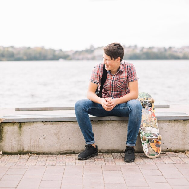 Adolescent avec planche à roulettes sur un banc près de l&#39;eau