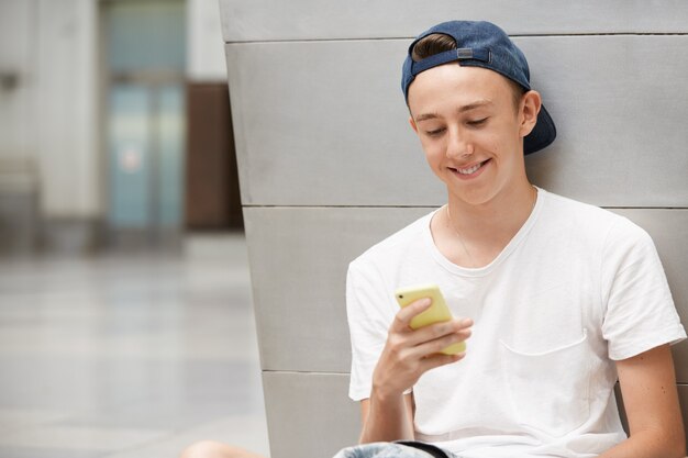 Photo gratuite adolescent portant une casquette et à l'aide de smartphone