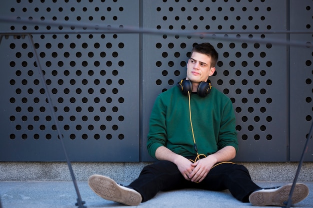 Adolescent de sexe masculin avec un casque assis sur le sol et se penchant en arrière avec les jambes écartées