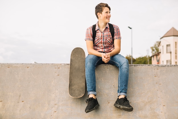 Photo gratuite adolescent avec skateboard assis sur le mur de béton