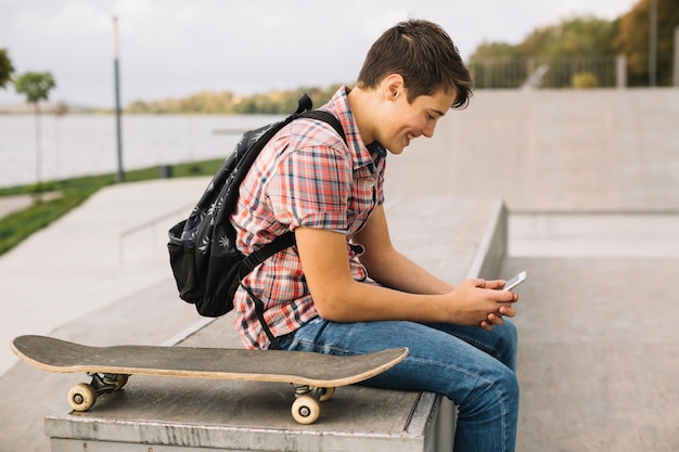 Adolescent avec smartphone assis près de la planche à roulettes