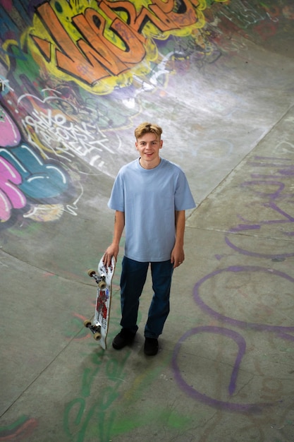 Adolescent souriant à angle élevé tenant une planche à roulettes