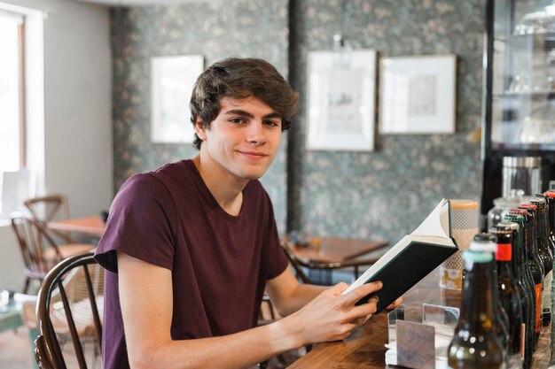 Adolescent souriant avec livre au comptoir du café