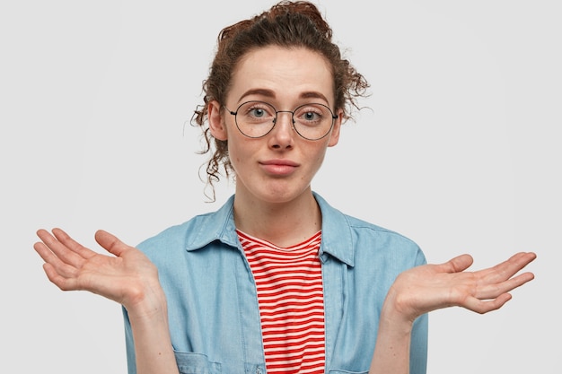 Photo gratuite adolescent de taches de rousseur perplexe avec des lunettes posant contre le mur blanc