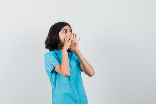 Adolescente appelant quelqu'un avec une voix forte en chemise bleue et à la recherche concentrée.