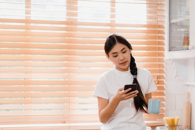 Adolescente asiatique jeune femme buvant du café chaud à l&#39;aide de la musique d&#39;écoute smartphone et vérification sociale