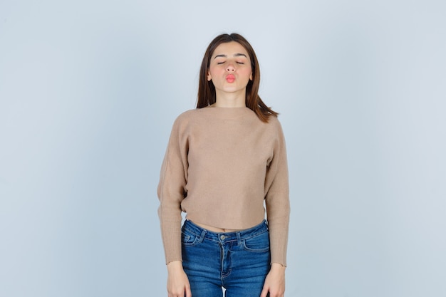 Une adolescente boudant les lèvres, fermant les yeux dans un pull, un jean et l'air tentante, vue de face.