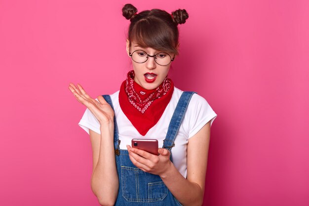 Une adolescente choquée tient un téléphone portable moderne, a un message avec de mauvaises nouvelles de son amie, perplexe. Une fille bouleversée regarde un téléphone intelligent, voit que son petit ami n'est pas en ligne. Concept technologique.