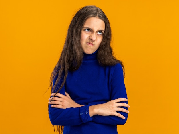 Adolescente confuse debout avec une posture fermée levant isolée sur un mur orange avec espace de copie