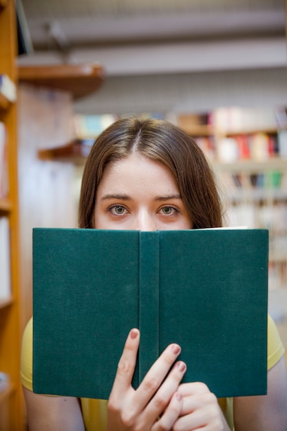 Adolescente couvrant le visage avec un livre dans la bibliothèque