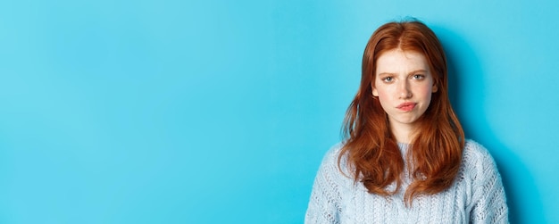 Photo gratuite adolescente déçue aux cheveux rouges en fronçant les sourcils et en souriant mécontent à la position de jugement