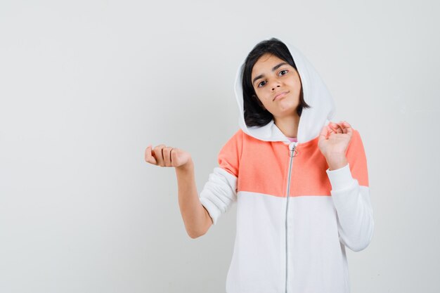 Adolescente écartant les paumes de côté en sweat-shirt et regardant hésitante.