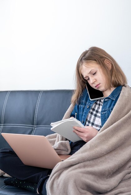 Une adolescente est assise sur le canapé devant un ordinateur portable et parle au téléphone