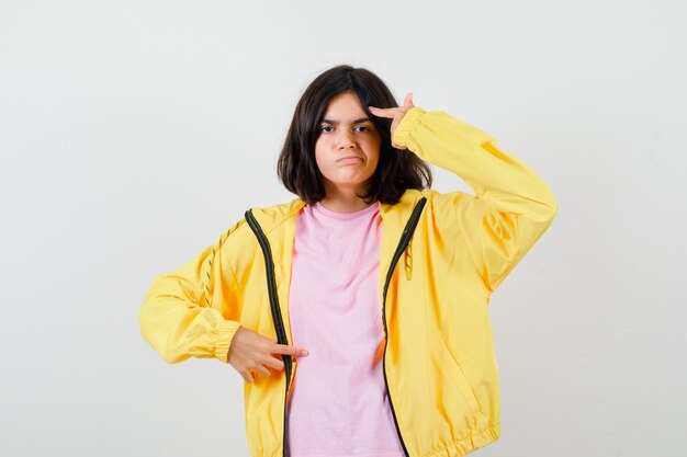 Une adolescente faisant un geste de suicide en t-shirt, une veste jaune et l'air agacée. vue de face.