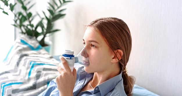Une adolescente fait de l'inhalation avec un équipement de nébulisation. enfant malade tenant un inhalateur à la main et respire à travers un inhalateur à la maison