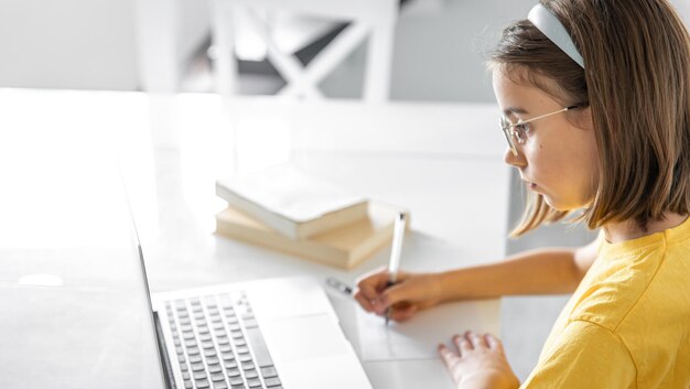 Une adolescente fait ses devoirs assise avec des livres et un ordinateur portable