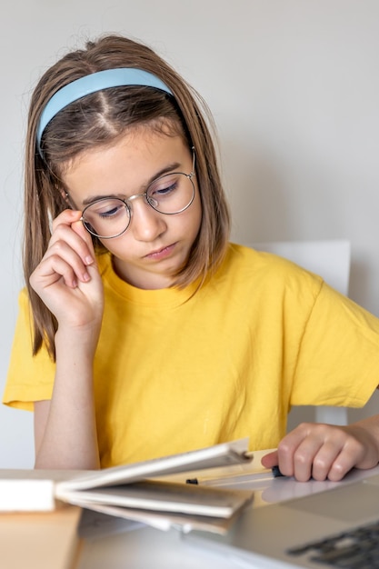 Photo gratuite une adolescente fait ses devoirs avec des livres et un ordinateur portable assis à une table