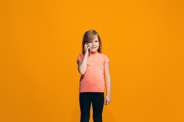 L'adolescente heureuse debout et souriant contre l'espace orange.