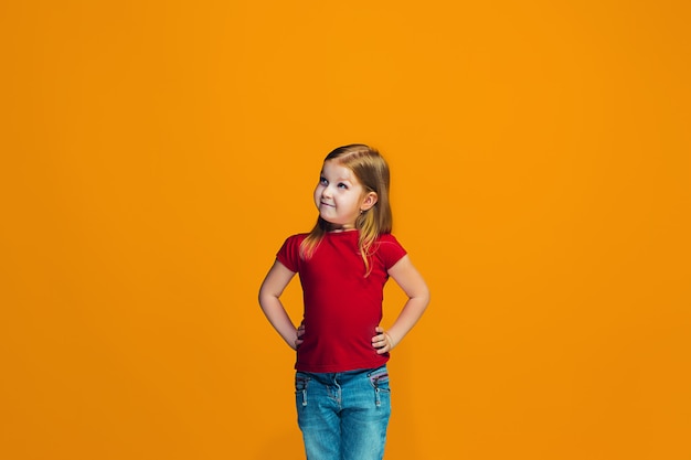 L'adolescente heureuse debout et souriant contre l'espace orange.